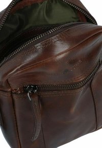Brown leather bag with a zippered opening, interior lined in dark green fabric, featuring visible stitching and an exterior zip pocket.