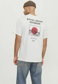 White cotton t-shirt with a graphic design featuring a red sun and mountains on the back, text reading "ROYAL DENIM DIVISION," relaxed fit.