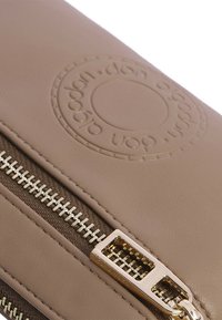 Estuche de cuero sintético marrón con cremallera, logotipo emblema, hardware de cremallera en tono dorado y textura suave. Forma compacta y rectangular.