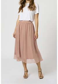 Ljusrosa, flödande midi kjol av genomskinligt tyg med elastisk midja, ihop med en enkel vit t-shirt och sandaler med remmar.