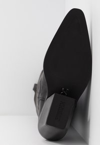 Czarny skórzany botek za kostkę z szerokim obcasem typu blok, teksturowaną podeszwą i elegancką sylwetką. Z boku ozdobiony klamrą.