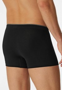 Black boxer briefs made of smooth fabric, featuring a contrasting waistband and a fitted design that provides full coverage.