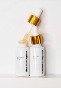 Biolumin-C-Serumfläschchen aus weißem Glas mit matter Oberfläche, goldenen Akzenten und Pipetten; klarer Inhalt; Etiketten mit schwarzem Text.