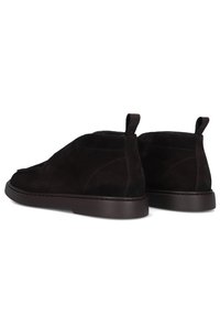 Een paar donkergroene suède enkelboots met trekhaakjes en platte rubberen zolen, weergegeven vanuit een achteraanzicht op een witte achtergrond.