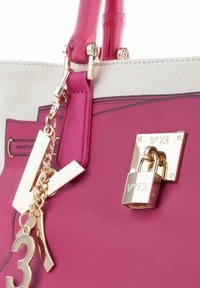 Roze leren handtas met een gouden slotdetail. Heeft canvas accenten, gouden hardware, kettingversiering en een groot metalen nummer '3'.