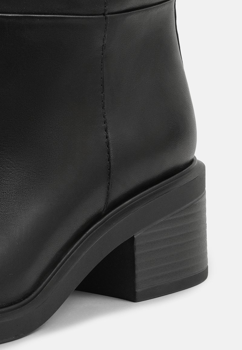 Stivaletto in pelle nera con punta rotonda, tacco a blocco spesso e dettagli di cucitura sobria lungo la cucitura. Texture liscia.