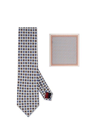 Krawat z jedwabiu oraz pasująca poszetka z powtarzającym się niebiesko-brązowym kwiatowym wzorem na białym tle, poszetka ma czerwoną i białą obwódkę.