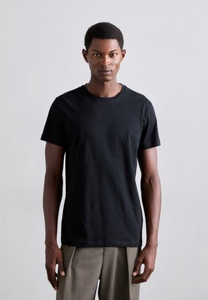 Tricou din bumbac negru cu guler rotund și mâneci scurte, având o croială clasică. Purtați-l cu pantaloni gri deschis. Design simplu, fără modele.