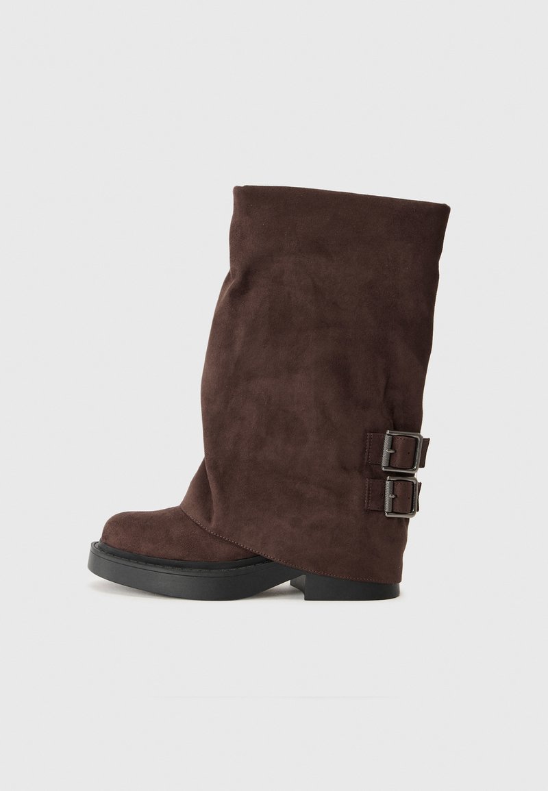 Brauner Wildlederschuh mit einem lässigen Design, ausgestattet mit zwei silbernen Schnallen an der Seite und einer flachen schwarzen Gummisohle.