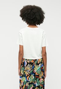 White cropped t-shirt with short sleeves, paired with a colorful, patterned skirt featuring tropical leaf designs in various colors.