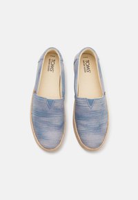 Kék vászon slip-on cipők vízszintes csíkokkal, texturált felsőrésszel és természetes juta talppal. Belsején márkajelzés látható.
