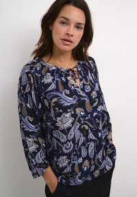 Blusa blu navy con motivi floreali e paisley, caratterizzata da un colletto rotondo con lacci e maniche a 3/4. Tessuto morbido con una vestibilità rilassata.