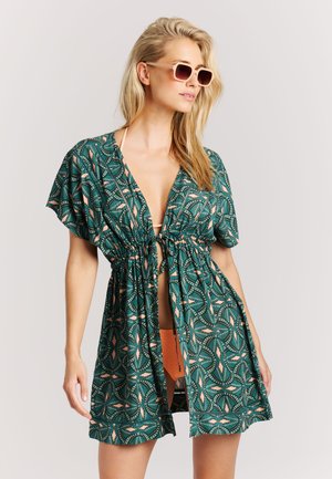 Groen kaftan met patroon en striksluiting, korte mouwen en een diepe V-hals. Het materiaal is lichtgewicht; bevat een mix van abstracte vormen in koraalkleur.
