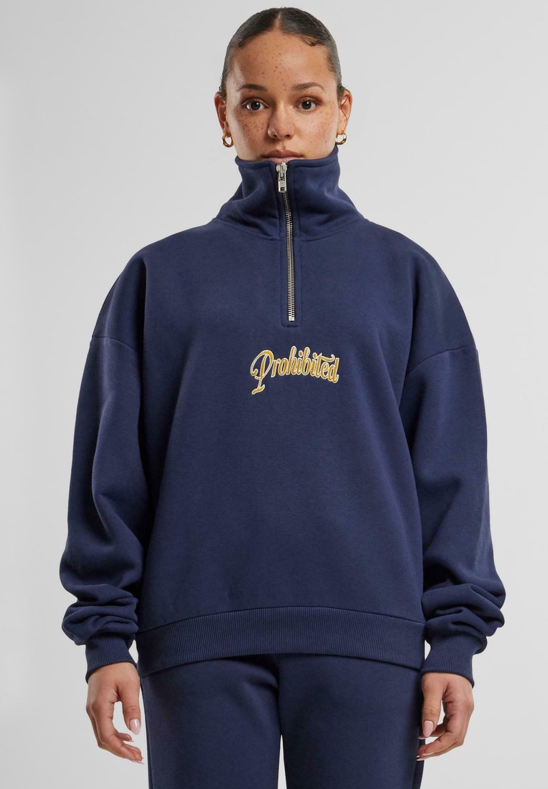 Maglione a collo alto di colore blu navy con zip frontale e logo "Proibito" ricamato in oro. Presenta una vestibilità comoda e polsini a coste.