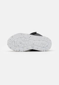 Schwarzer Sneaker mit strukturiertem Obermaterial und Klettverschluss, ausgestattet mit einer weißen Gummisohle mit schwarzen Sprenkeln und einem gemusterten Profil.
