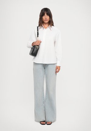 White button-up shirt with long sleeves, paired with light blue wide-leg jeans and black handbag featuring a gold circular accent.
