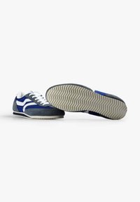 Zapatillas de ante en color marino y gris con franjas blancas, suelas de goma texturizadas y un diseño clásico de cordones. Estilizadas con un perfil bajo y un patrón de espiga.