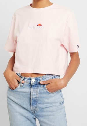 Person wearing a light pink cropped t-shirt with white logo and light blue high-waisted jeans with hands in pockets.