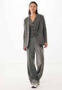 Traje gris de tres piezas que incluye un blazer ajustado, un chaleco con botones y pantalones de pierna ancha, fabricado en una tela texturizada.