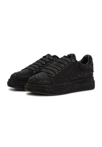 Paire de baskets noires basses avec semelles compensées épaisses, larges lacets noirs et embellissements en strass scintillants sur toute la surface.