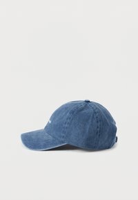 Gorra de mezclilla con visera curva, textura suave y color azul claro. Presenta un logo bordado, ojales cosidos y una correa ajustable en la parte trasera.