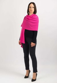 Lysende pink sjal lavet af blødt stof, draperet elegant omkring skuldrene, parret med en sort top og tætsiddende sorte bukser.