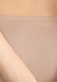 Slip beige senza cuciture di Sloggi con texture a costine, caratterizzato da una fascia in vita morbida e un marchio discreto. Tessuto liscio e elasticizzato.