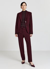 Completo bordeaux a righe con blazer attillato e pantaloni dritti, abbinato a un top in maglia scuro e tacchi a punta.