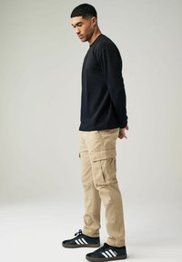 Cămașă neagră cu mâneci lungi, pantaloni cargo bej și adidași negri cu dungi albe. Stilizat cu o croială lejeră și o textură netedă.