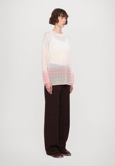Pulover transparent din tricot cu un gradient de la alb la roz, având un model în zigzag. Asortat cu pantaloni largi cu model chevron în nuanțe de maro.