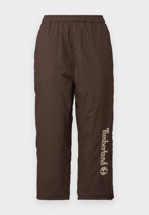 Calças de nylon castanhas com um cós elástico. Apresenta um logótipo vertical da Timberland em bege claro. Textura suave, fechos de zíper nos tornozelos para ajuste.