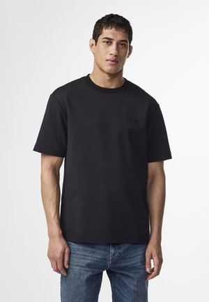 Black crew neck t-shirt with short sleeves, made of a smooth fabric. Features subtle embossed text on the chest and a relaxed fit.