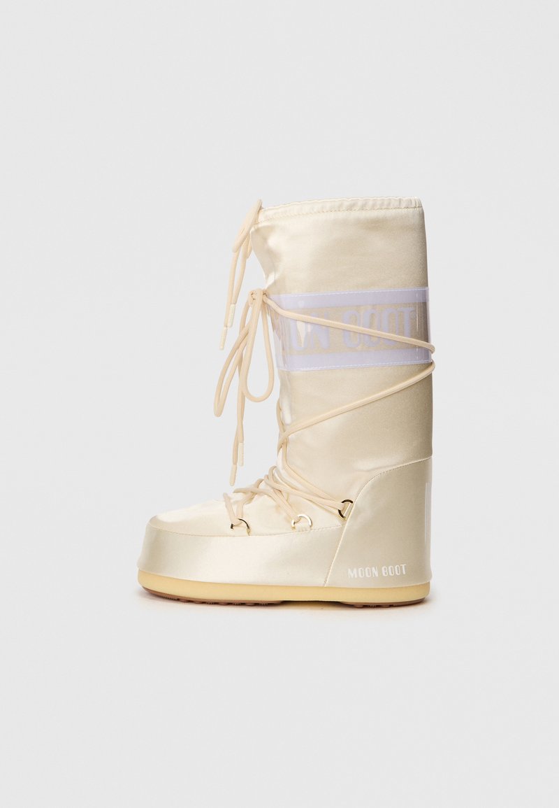 Bottines Moon beige avec finition satinée, présentant un design à lacets, un tige rembourrée et une semelle en caoutchouc. Les accents comprennent une bande transparente avec logo.