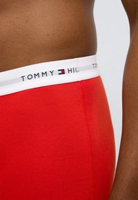 Κόκκινα βαμβακερά ανδρικά μποξεράκια με λευκή ελαστική ζώνη μέσης με μαύρο και γκρι λογότυπο. Ομαλή υφή με επίπεδες ραφές.