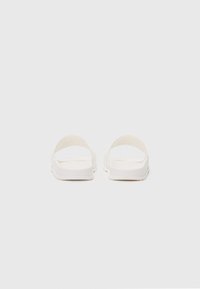 Witte instap sandaal met een rond ontwerp, platte zool en minimalistische banden, met een gladde textuur en zonder zichtbare hardware.