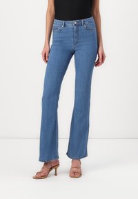 Mørkeblå flared jeans med høy midje, som har fem lommer og en glatt denimstruktur. Komplimentert av lysebrune hæler med stropper.