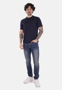 T-shirt a maniche corte blu scuro abbinato a jeans aderenti blu, completato da sneakers bianche. Tessuto morbido e vestibilità casual.