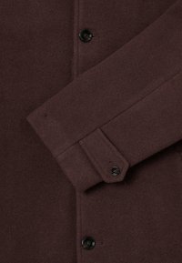 Brown wool coat with a soft texture, featuring a buttoned cuff and two black buttons on the front for closure.