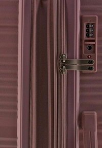 Hard-shell suitcase in a muted pink hue with vertical ribbed texture, secure zipper closure, and integrated combination lock.