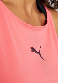 Różowy sportowy tank top z okrągłym dekoltem, wykonany z lekkiego, oddychającego materiału. Na środku znajduje się czarne logo Puma.