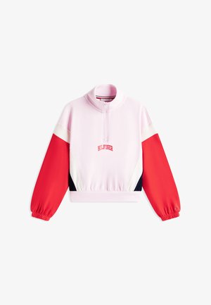 Vaatteena pinkki collegetakki, jossa korkea kaulus ja puoliksi vetoketjullinen malli. Hihat ovat punavalkoiset väriblokit, ja helmassa on resori. Edessä on "HILFIGER"-logo.