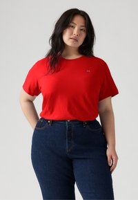 T-shirt rosso a maniche corte in morbido cotone con scollo a girocollo, caratterizzato da un piccolo logo sul petto. Abbinato a jeans scuri a vita alta.