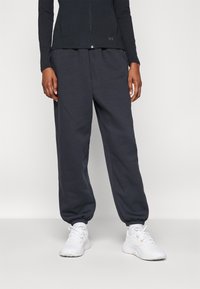 Dunkelgraue Sweatpants mit elastischen Bündchen, aus weichem Stoff, kombiniert mit weißen Sportschuhen. Der Bund ist elastisch für mehr Komfort.