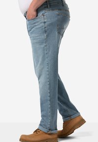Jeans de mezclilla azul claro con corte recto. Presentan dos bolsillos laterales, un bolsillo trasero y puños enrollados; se combinan con botas de trabajo color tostado.
