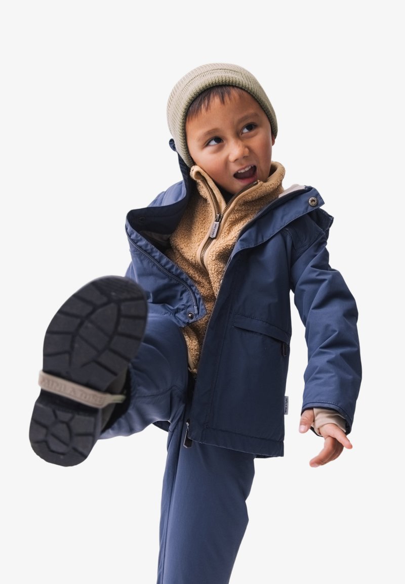 Marine blauwe waterdichte jas met een rits, beige fleece voering en bijpassende broek. Voorzien van een gebreide muts, verhoogde kraag en een gestructureerde zool.