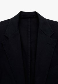 Blazer negro con un diseño clásico de solapa tipo muesca. Presenta hombros estructurados y una textura suave. Detalles minimalistas, sin herrajes visibles.