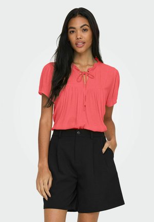 Koraleowa bluzka z krótkimi rękawami, z ozdobnym wiązaniem przy dekolcie, zestawiona z czarnymi szortami o wysokim stanie z kieszeniami i dopasowanym krojem.