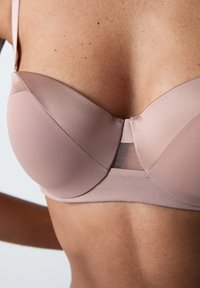 Reggiseno imbottito in morbido tessuto beige con una finitura liscia; presenta dettagli in rete nella parte posteriore e un design strutturale per il supporto.