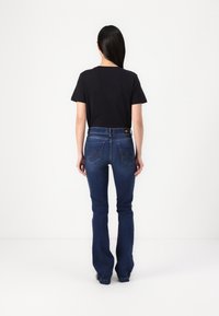 Jeans de campana azul oscuro combinados con una camiseta negra de manga corta, vistos desde atrás. Textura de denim suave, diseño minimalista.