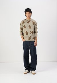 Beige sweater with brown gingerbread man pattern, round neckline, long sleeves; paired with dark blue loose jeans and white sneakers.